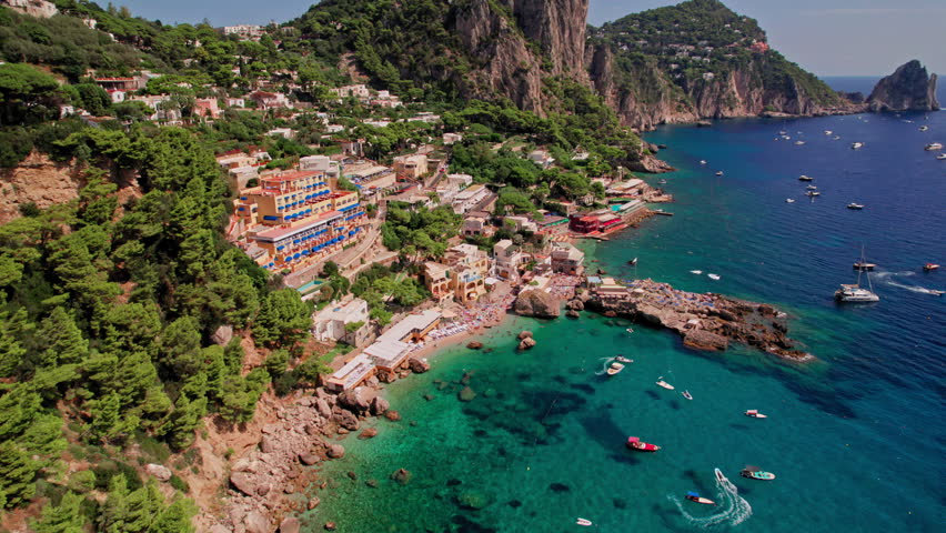 A cinematic aerial shot of the beautiful cliffs and beach landscape of Marina Piccola on the island of Capri, a popular tourist destination along the Amalfi Coast in the Bay of Naples in Italy. Royalty-Free Stock Footage #1101115363