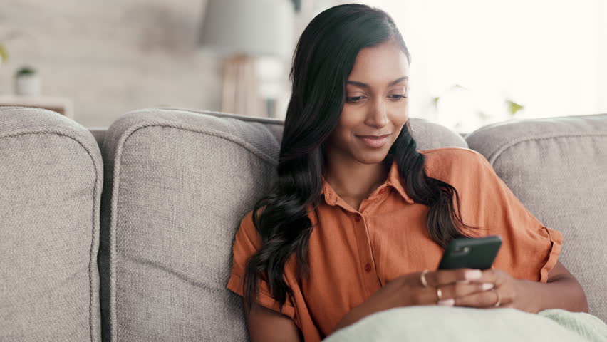 Woman, phone and smile for chatting on living room sofa in communication, texting or social media at home. Happy female relaxing and smiling on smartphone for networking, browsing or chat on couch | Shutterstock HD Video #1101116339
