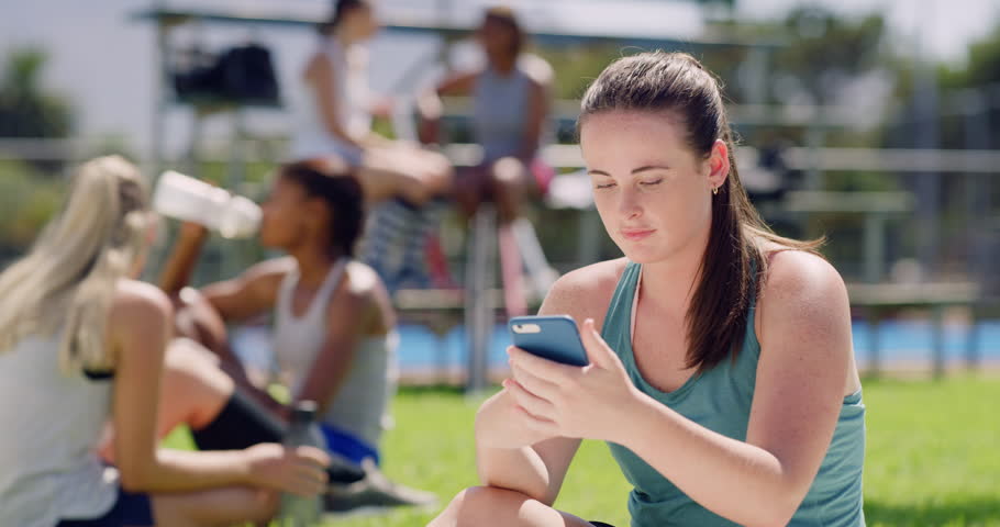 Young hockey player smiling and texting on a phone, checking social media. Teenage girl sitting, taking a break, using technology to browse and search the internet during training. Taking a screenshot