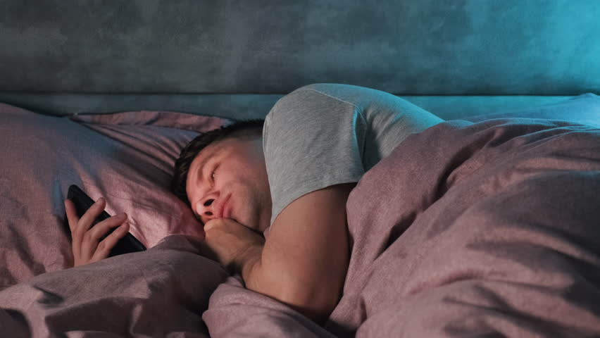 Man with mobile phone lying on his bed in the dark while scrolling smartphone and fall asleep. Surfing internet, social media at night | Shutterstock HD Video #1101117845