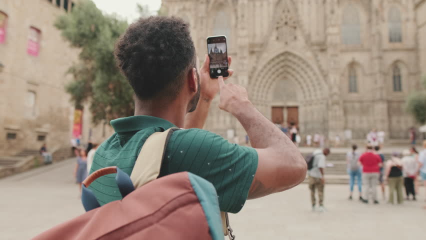 Young man tourist takes photo on cellphone while standing on the square of the old city. Back view Royalty-Free Stock Footage #1101118123