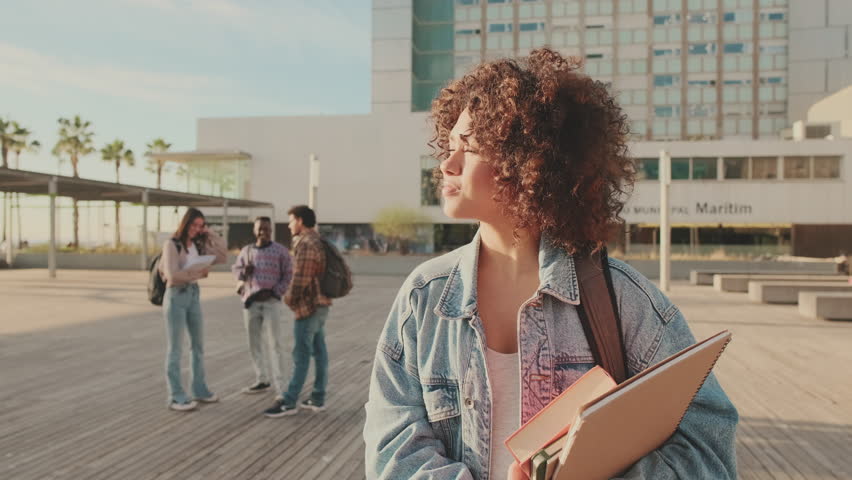 Girl is smiling while looking at the camera. Student with notebooks in her hands looks at the camera and smiles