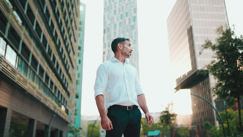 Mature businessman with neat beard wearing white shirt stands in the financial district in the city. Successful man looks around on modern buildings background Royalty-Free Stock Footage #1101118157