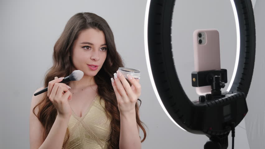Beautician gives makeup lessons to followers teaching to apply powder. Lady blogger broadcasts online on social networks via smartphone closeup Royalty-Free Stock Footage #1101121645