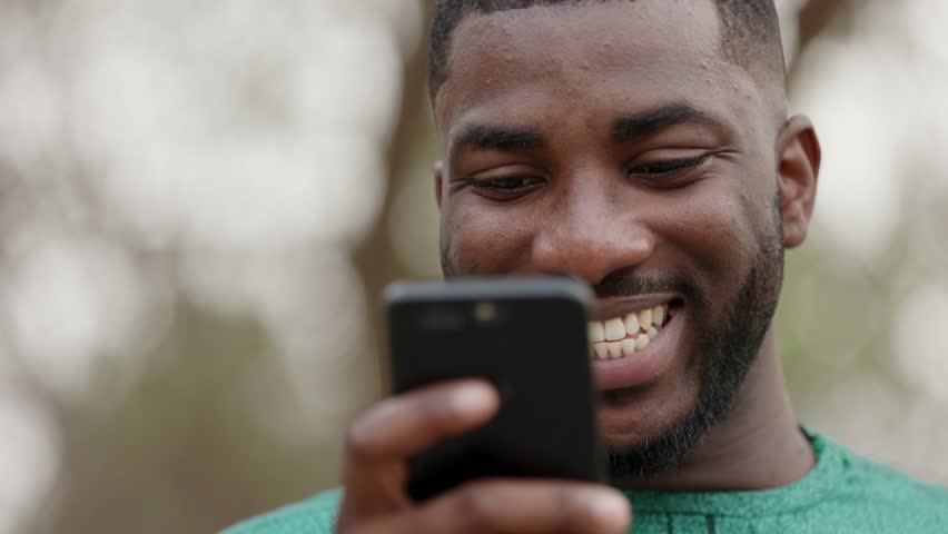 Smiling Young African Man holding smartphone, checks prices of medicine in online pharmacy, books doctors appointment in health facility. Close Up. Royalty-Free Stock Footage #1101122913