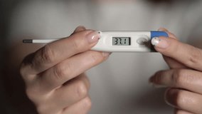 A woman holds a thermometer in her hands to measure body temperature. 39 degrees Celsius. Doctor or nurse, sick patient. Fever from Covid-19 virus. Deadly diagnosis. Coronavirus pandemic, flu epidemic - Powered by Shutterstock - Get 15% off with code: PIKWIZARD15