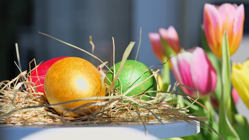Easter colorful eggs rotate in nest in hey outdoor in sunny warming day, tulips flower background. Happy Easter holiday. Christian celebration, family traditions. Selective focus