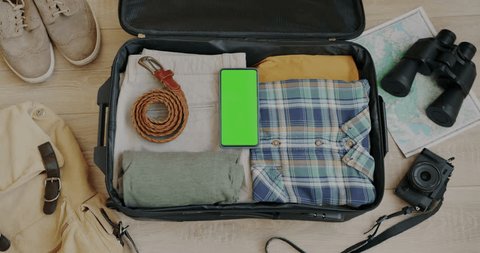 Top view of male hand packing clothes plane ticket passport and green screen chroma key smartphone in suitcase for journey. Tourism and luggage preparation concept. Adlı Stok Video