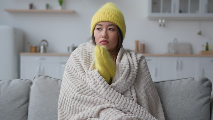 Frozen sick Asian woman suffer from cold low temperature at home feel freezing ethnic korean japanese girl covered blanket hat and mittens has covid-19 virus in winter heating problem cold flat froze Royalty-Free Stock Footage #1101131071