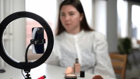 makeup tutorial beauty blogging, technology and people concept portrait of a happy smiling girl blogger with ring light and smartphone applying make up at home. making a influencer video Using brush