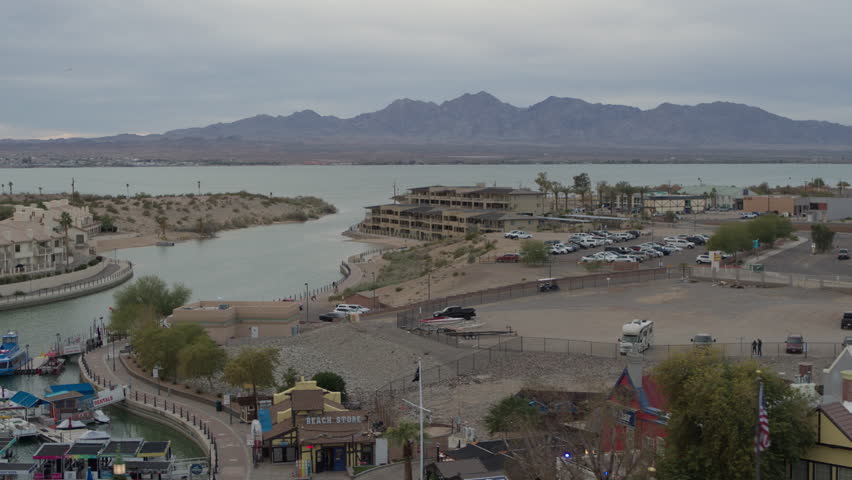 Aerial above parking lots and hotels on shore of Lake Havasu Arizona on cloudy day with mountains in background