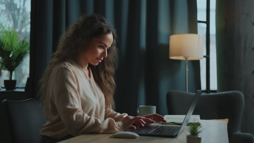 Shot of focused young Caucasian woman in elegant beige blouse using laptop, chatting with clients. Attractive concentrated girl working on social media marketing. Online work. Remote job. Professional | Shutterstock HD Video #1101136697