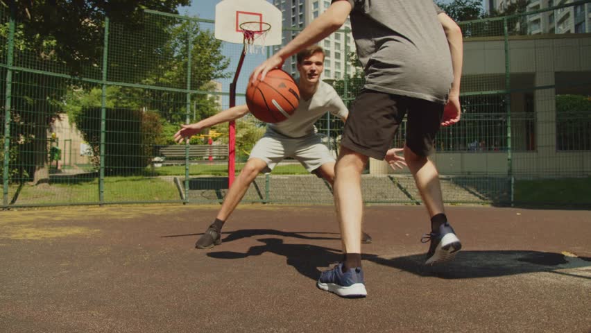 People playing street basketball during a warm summer day. Two teens playing a basketball match on an outdoors court during a sunny summer day. Attack and defence, missed shot. Royalty-Free Stock Footage #1101137295