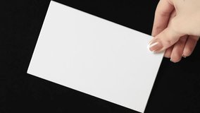 Vertical video. White card. Empty note. Invitation letter. Female hand showing clean mockup paper sheet with copy space on black background loop. - Powered by Shutterstock - Get 15% off with code: PIKWIZARD15