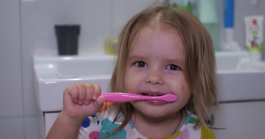 Child girls brush their teeth and indulge in the bathroom before going to bed. Little cute girl brushes her teeth funny while looking at the camera. The concept of independent children. Royalty-Free Stock Footage #1101137935