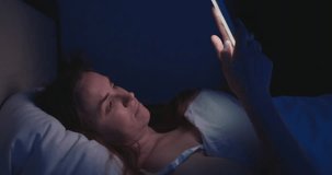 A woman lies in bed at night and uses a smartphone. Female using mobile phone