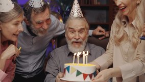 Elderly Man in Birthday Hat Blowing Out Candle on Birthday Cake, Celebrating Together with Other Senior People at Nursing Home. Birthday Party, Old Friends Blowing Party Horns. S3niorLife - Powered by Shutterstock - Get 15% off with code: PIKWIZARD15
