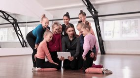 Young woman, gymnastics coach showing little girls, children video on tablet. Training session indoors. Concept of sportive lifestyle, childhood, education, health, professional sport.