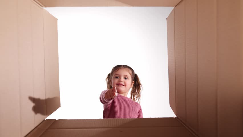 Little happy girl, child unpacking, opening cardboard box with happy smiling face. Good surprise, gift. Cheerful kid. Concept of shopping, delivery, emotions and facial expression
