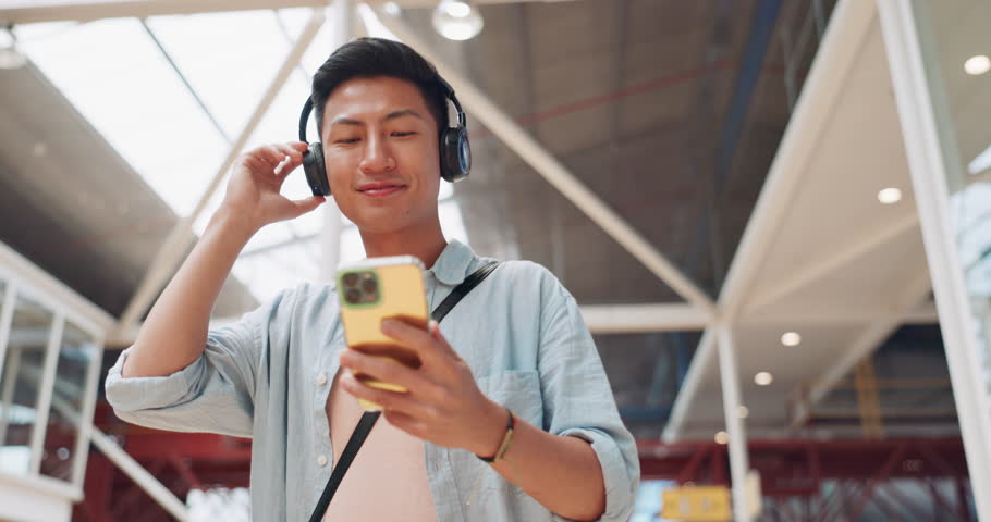 Asian man, phone and headphones for listening to music and dancing while walking in creative office with smile, happiness and positive mindset. Male entrepreneur during travel with network connection Royalty-Free Stock Footage #1101149077