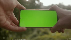 Close-Up of a Green Screen Smartphone Held Horizontally in Nature