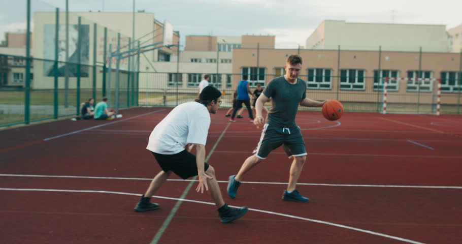 Concentrated friends playing basletball at playground man tries to make slam dunk competition time guy plays training shows skills .