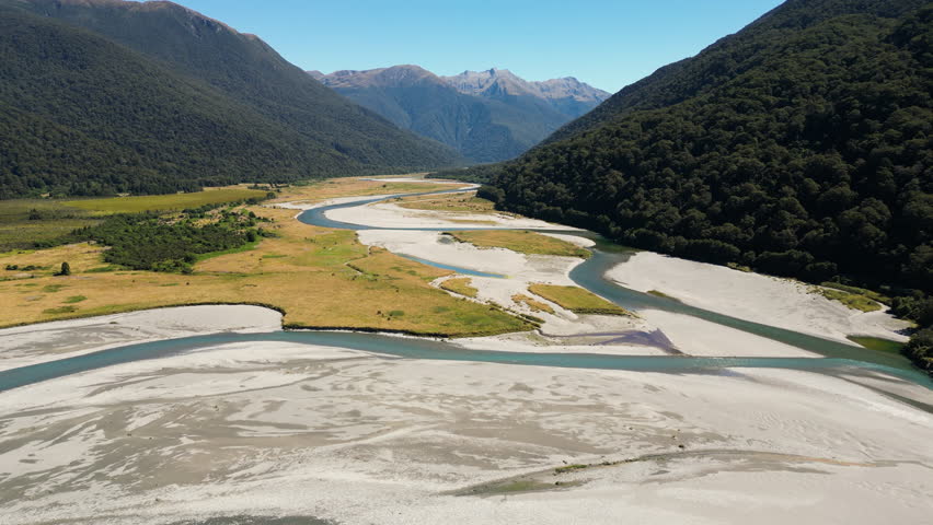 aerial scenic view of stunning New Zealand NZ landscape with river stream clean pristine water leading to mountains during clear sky sunny weather