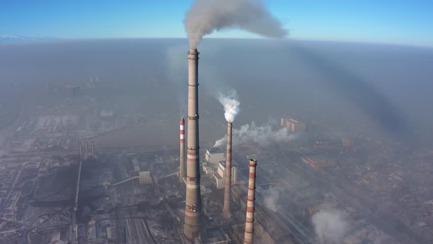 Aerial view of the pipes of the factory smoking and polluting the environment against the backdrop of a city covered in black smog