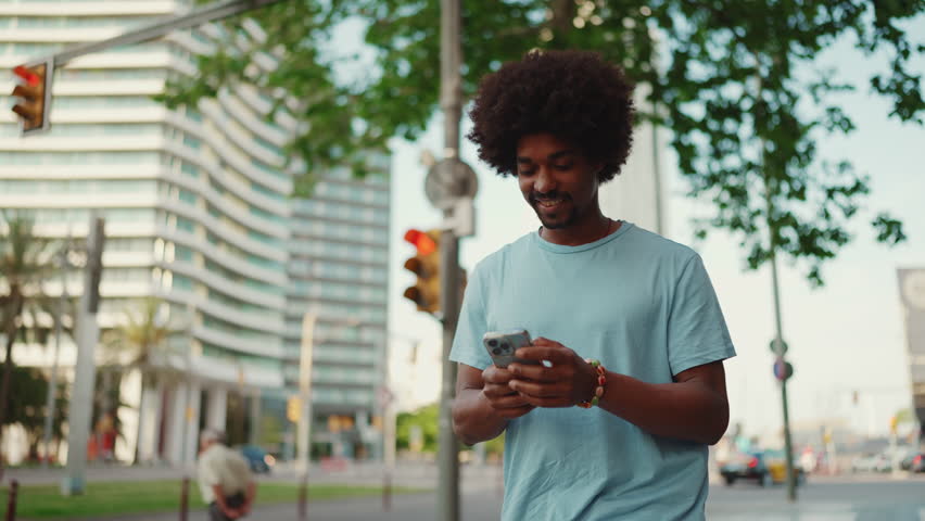 Closeup young man in light blue t-shirt goes on the street of modern city and holding smartphone looking at phone screen look for address with electronic map in city. slow motion