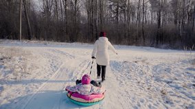 Mother and daughter sliding on snow tube at winter woods outdoors. Two females persons sledding and having fun outside. Woman running. Winter sports and leisure activity with healthy lifestyle