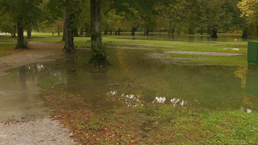Beautiful park area flooded due to increased river level after heavy autumn rain. Muddy floodwaters spilled boldly over river banks and overflowed lawns and trees. Severe flooding in the fall season.