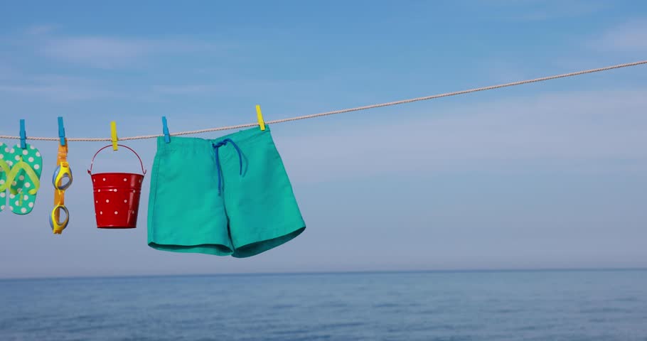 Beach objects hanging on a clothesline. Items for vacation against blue sky and sea. Summer holiday and travel concept. Slow motion | Shutterstock HD Video #1101173321