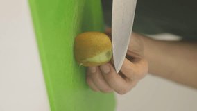 A man cuts the peel off a kiwi, vertical video