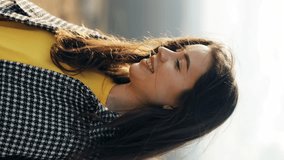 
Portrait of a woman enjoying nature on the mountain. Attractive woman looks forward and then at the camera and smiles. the wind blows the hair. Happy look, feeling of freedom. Vertical video orientat
