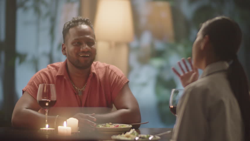 Cheerful couple smiling and chatting over dinner while having romantic date in evening at home