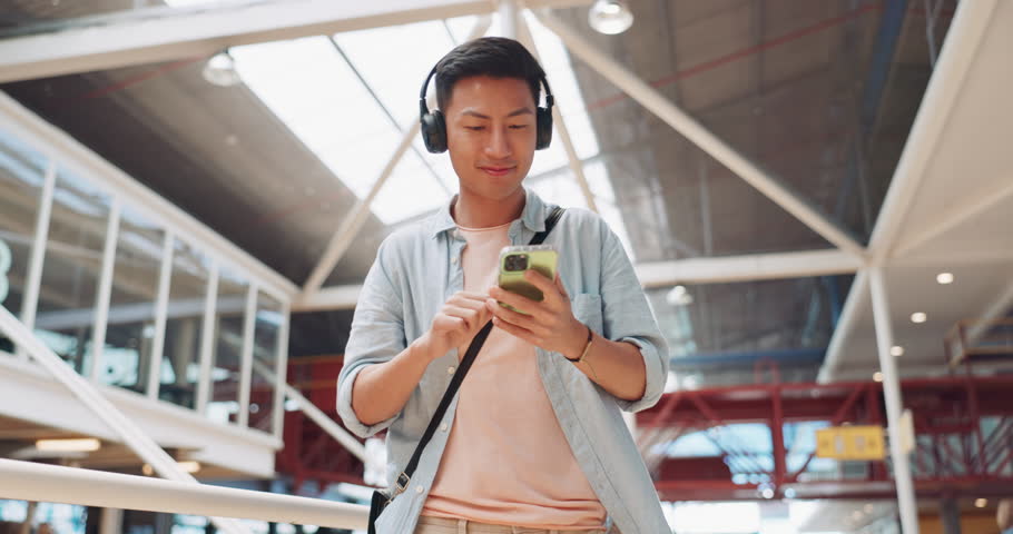 Phone, music headphones and Asian man walking in mall streaming podcast or radio. Technology, travel and happy male listening to song, audio sound or playlist on mobile smartphone in urban building. Royalty-Free Stock Footage #1101191171
