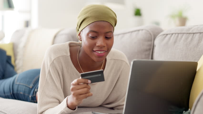 Laptop, credit card and excited black woman on a sofa while doing online shopping in her home. Happy, ecommerce and African female buying clothes on retail store website with computer while relaxing.