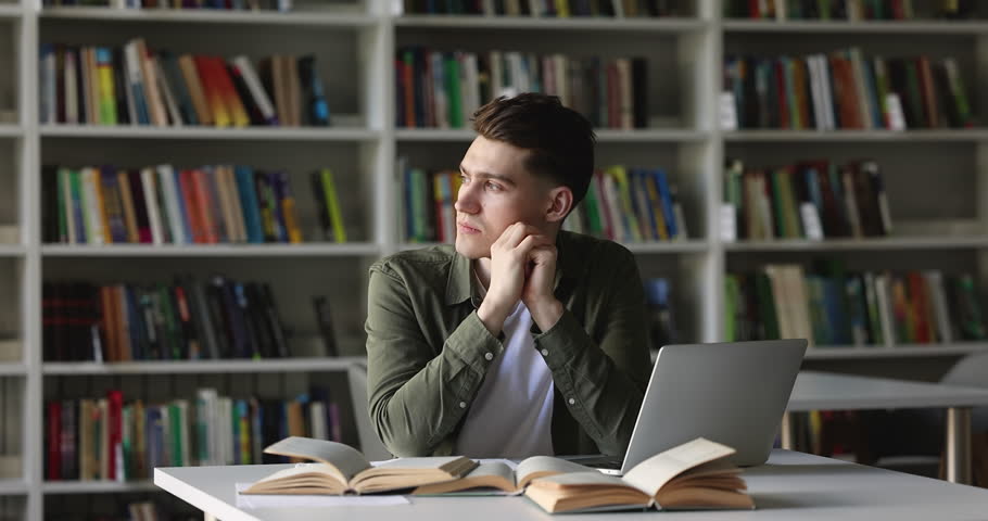 Serious college student guy thinking on project, looking away, using laptop in library, reading open books, textbook, writing notes, summary, working on research study, class report Royalty-Free Stock Footage #1101193053