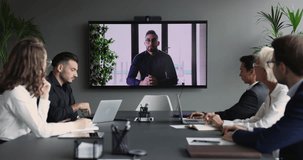 Corporate staff members, businesspeople listen to boss speaks from TV screen during video conference, talk about investment strategy, share goal, sales result. Group teleconference event in boardroom