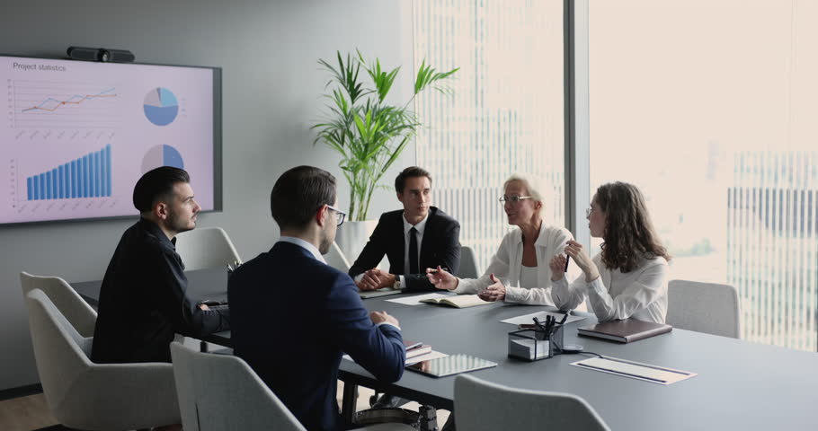 Group of businesspeople, investors sit at desk engaged in financial analysis, negotiations, discussing finances, make forecast of trade results shown in graphs and diagrams on TV screen in boardroom Royalty-Free Stock Footage #1101193129