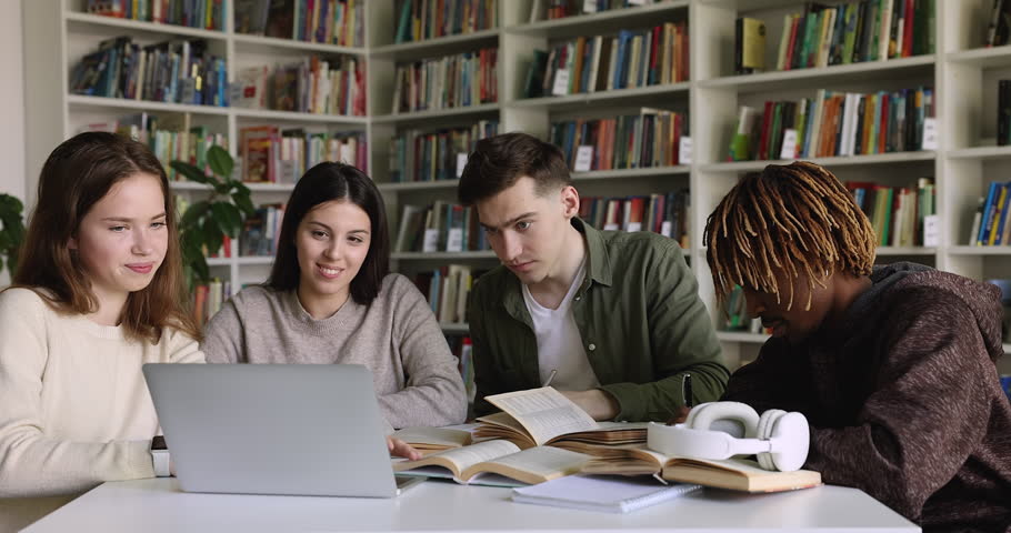 Multiethnic group of teen gen Z students watching virtual class, online learning presentation in library, attending conference, webinar, talking, discussing video at laptop and open books Royalty-Free Stock Footage #1101193191