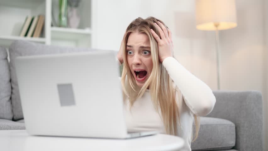 Nervous stressed young blond woman freelancer typing quickly on laptop computer and looking at clock in her hands asking to hurry up scream and warning about deadline at home