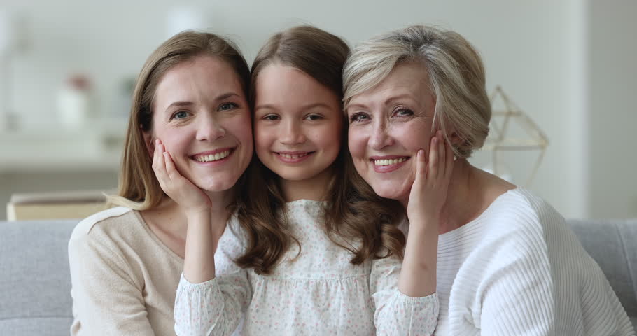 Happy sweet daughter kid touching cheeks, faces of mother and senior grandma. Little girl, mom, grandmother sitting together on home sofa, hugging, looking at camera, smiling. Family portrait | Shutterstock HD Video #1101194813
