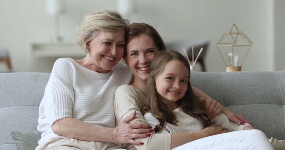 Cheerful excited kid girl, mother and grandma enjoying emotional meeting, family bonding, leisure together, resting on home couch, hugging, talking, chatting, laughing, looking at camera Royalty-Free Stock Footage #1101194821