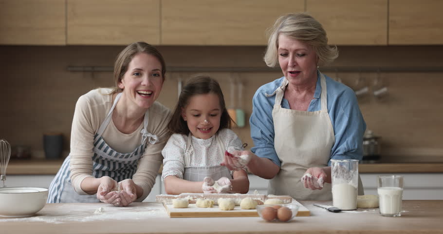 Excited cheerful girl, mom and grandma baking together in home kitchen, having fun, clapping floury hands, making messy cloud of flour, laughing at table with bakery food ingredients Royalty-Free Stock Footage #1101194827