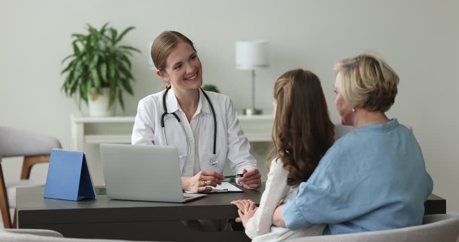 Happy pediatrician doctor talking to mature grandmother and patient girl with toy, sitting at workplace table, listening, smiling. Senior woman and grandkid visiting family physician Royalty-Free Stock Footage #1101194845