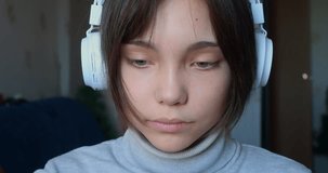 Face of a teenage girl in headphones in front of a computer monitor - she communicates online, smiles and exchanges messages. Youth culture of online communication. 60 fps 4k footage.