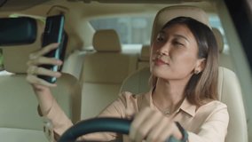 Young Asian businesswoman chatting via video call on smartphone while sitting on driver seat in car