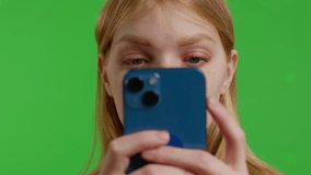 Extreme close-up of an Attractive red-haired Caucasian woman texting or reading on her handheld mobile cell phone with focus on eyes. on a green background in the studio. 4k uhd