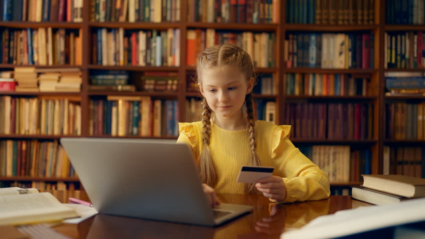 Happy schoolgirl making purchase on laptop using credit card, online shopping